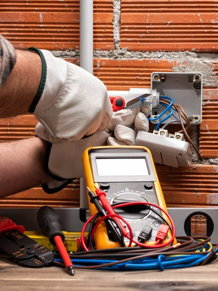 Electrician worker at work with scissors prepares the electrical cables of an electrical system. Working safely with protective gloves. Construction industry.