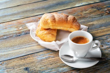 Yukarıdan bak. Açık mavi ahşap arka planda bir fincan sıcak İtalyan espresso kahvesi ve kruvasan. Yiyecek ve içecek. Yaşam biçimi.