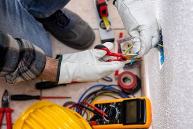 Yukarıdan bak. Makasla çalışan elektrik işçisi elektrik sisteminin elektrik kablolarını hazırlıyor. Koruyucu eldivenlerle güvenli bir şekilde çalışmak. İnşaat endüstrisi.