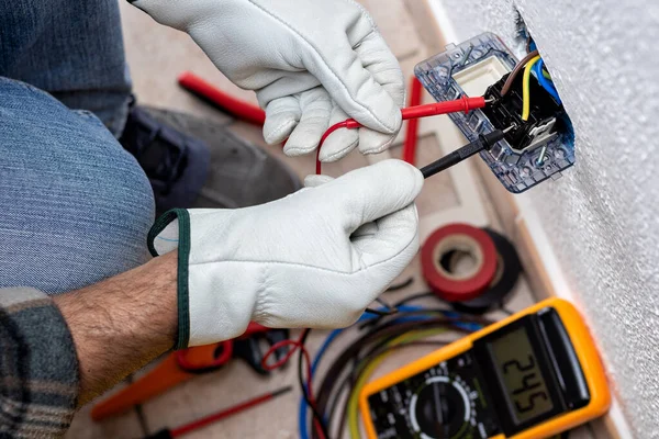 View from above. Electrician worker at work with the tester measures the voltage in an electrical system. Working safely with protective gloves. Construction industry.