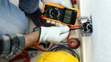 Yukarıdan bak. Elektrikçi, test ediciyle çalışırken elektrik sistemindeki voltajı ölçer. Koruyucu eldivenlerle güvenli bir şekilde çalışmak. İnşaat endüstrisi. Görüntü.