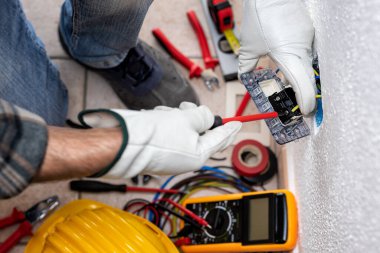 Yukarıdan bak. Tornavidayla çalışan elektrik işçisi elektrik sisteminin prizlerindeki elektrik kablolarını tamir ediyor. Koruyucu eldivenlerle güvenli bir şekilde çalışmak. İnşaat endüstrisi.