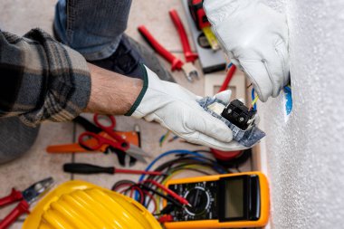 Yukarıdan bak. Elektrik işçisi elektrik sisteminin prizlerine elektrik kabloları yerleştiriyor. Koruyucu eldivenlerle güvenli bir şekilde çalışmak. İnşaat endüstrisi.