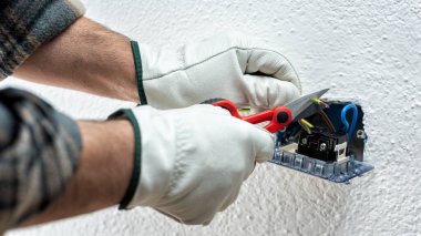 Makasla çalışan elektrik işçisi elektrik sisteminin elektrik kablolarını hazırlıyor. Koruyucu eldivenlerle güvenli bir şekilde çalışmak. İnşaat endüstrisi.
