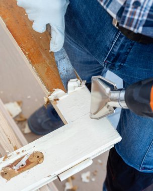 Marangoz ısı tabancası ve odun kazıyıcı kullanarak eski ahşap penceredeki boyayı temizler. İnşaat endüstrisi, marangozluk. Yenileme. 