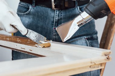 Marangoz ısı tabancası ve odun kazıyıcı kullanarak eski ahşap penceredeki boyayı temizler. İnşaat endüstrisi, marangozluk. Yenileme. 