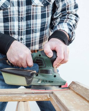 Zanaatkar. Yetişkin bir marangoz eski bir ahşap pencereyi düzeltmek için elektrikli zımpara makinesi kullanıyor. İnşaat endüstrisi, marangozluk, ev işi. Yenileme.