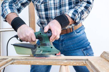 Zanaatkar. Yetişkin bir marangoz eski bir ahşap pencereyi düzeltmek için elektrikli zımpara makinesi kullanıyor. İnşaat endüstrisi, marangozluk, ev işi. Yenileme.