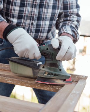 Zanaatkar. Yetişkin bir marangoz eski bir ahşap pencereyi düzeltmek için elektrikli zımpara makinesi kullanıyor. İnşaat endüstrisi, marangozluk, ev işi kendin yap, işyeri güvenliği. Yenileme.