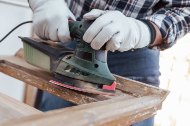 Zanaatkar. Yetişkin bir marangoz eski bir ahşap pencereyi düzeltmek için elektrikli zımpara makinesi kullanıyor. İnşaat endüstrisi, marangozluk, ev işi kendin yap, işyeri güvenliği. Yenileme.