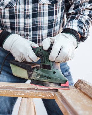 Zanaatkar. Yetişkin bir marangoz eski bir ahşap pencereyi düzeltmek için elektrikli zımpara makinesi kullanıyor. İnşaat endüstrisi, marangozluk, ev işi. Kendin yap. İş yeri güvenliği. Yenileme.