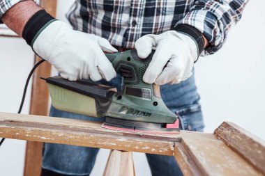 Zanaatkar. Yetişkin bir marangoz eski bir ahşap pencereyi düzeltmek için elektrikli zımpara makinesi kullanıyor. İnşaat endüstrisi, marangozluk, ev işi. Kendin yap. İş yeri güvenliği. Yenileme.