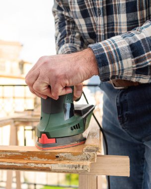 Zanaatkar. Yetişkin bir marangoz eski bir ahşap pencereyi düzeltmek için elektrikli zımpara makinesi kullanıyor. İnşaat endüstrisi, marangozluk, ev işi. Yenileme.
