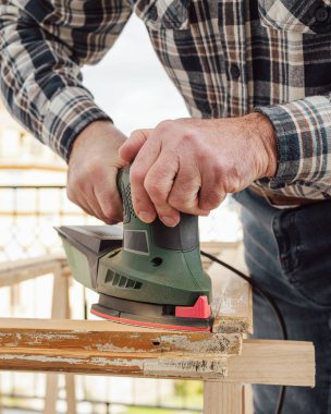 Zanaatkar. Yetişkin bir marangoz eski bir ahşap pencereyi düzeltmek için elektrikli zımpara makinesi kullanıyor. İnşaat endüstrisi, marangozluk, ev işi. Yenileme.