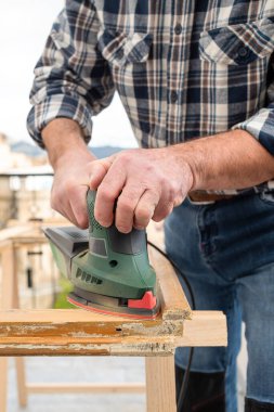 Zanaatkar. Yetişkin bir marangoz eski bir ahşap pencereyi düzeltmek için elektrikli zımpara makinesi kullanıyor. İnşaat endüstrisi, marangozluk, ev işi. Yenileme.