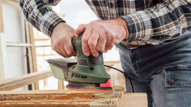 Zanaatkar. Yetişkin bir marangoz eski bir ahşap pencereyi düzeltmek için elektrikli zımpara makinesi kullanıyor. İnşaat endüstrisi, marangozluk, ev işi. Yenileme.