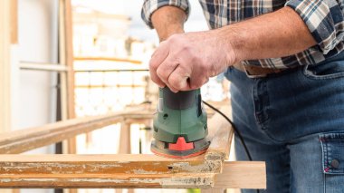 Zanaatkar. Yetişkin bir marangoz eski bir ahşap pencereyi düzeltmek için elektrikli zımpara makinesi kullanıyor. İnşaat endüstrisi, marangozluk, ev işi. Yenileme.