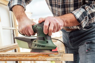 Zanaatkar. Yetişkin bir marangoz eski bir ahşap pencereyi düzeltmek için elektrikli zımpara makinesi kullanıyor. İnşaat endüstrisi, marangozluk, ev işi. Yenileme.