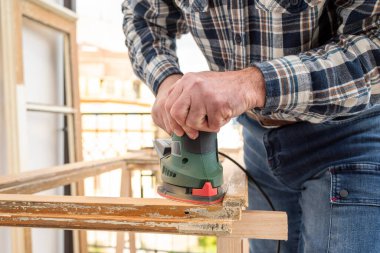 Zanaatkar. Yetişkin bir marangoz eski bir ahşap pencereyi düzeltmek için elektrikli zımpara makinesi kullanıyor. İnşaat endüstrisi, marangozluk, ev işi. Yenileme.