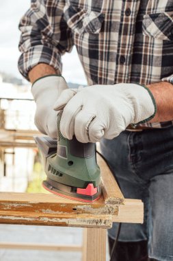 Zanaatkar. Yetişkin bir marangoz eski bir ahşap pencereyi düzeltmek için elektrikli zımpara makinesi kullanıyor. İnşaat endüstrisi, marangozluk, ev işi kendin yap, işyeri güvenliği. Yenileme.