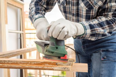Zanaatkar. Yetişkin bir marangoz eski bir ahşap pencereyi düzeltmek için elektrikli zımpara makinesi kullanıyor. İnşaat endüstrisi, marangozluk, ev işi kendin yap, işyeri güvenliği. Yenileme.