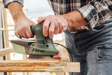 Zanaatkar. Yetişkin bir marangoz eski bir ahşap pencereyi düzeltmek için elektrikli zımpara makinesi kullanıyor. İnşaat endüstrisi, marangozluk, ev işi. Kendin yap. Yenileme.