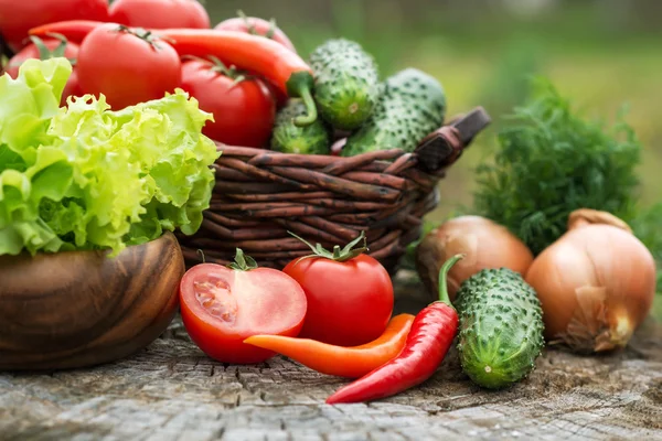 Basket and wooden plate with fresh vegetables (tomatoes, cucumbe — Stock Photo, Image