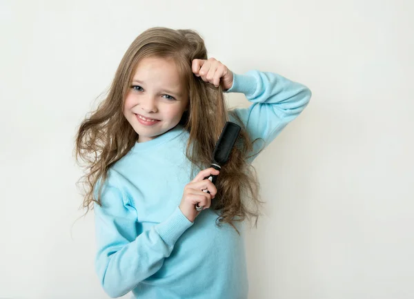 Cute smiling little girl combing her hair comb makes hair — Stock Photo, Image