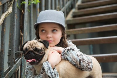 Little girl playing with her pug dog outdoors in rural areas clipart