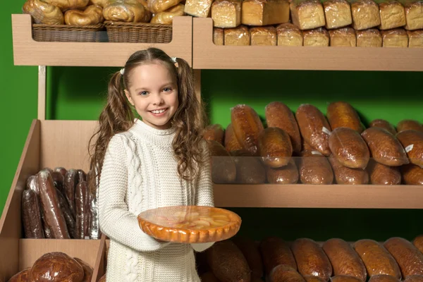Kleines Mädchen mit Brot in der Hand. Hintergrund der Brotregale . — Stockfoto