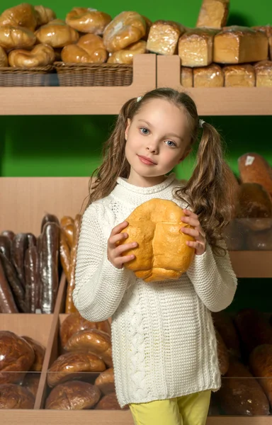 Kleines Mädchen mit Brot in der Hand. Brotregale im Hintergrund. s — Stockfoto