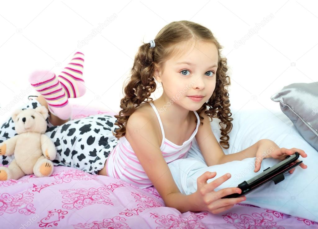 Heureuse petite fille couchée sur le lit avec tablette image libre de ...