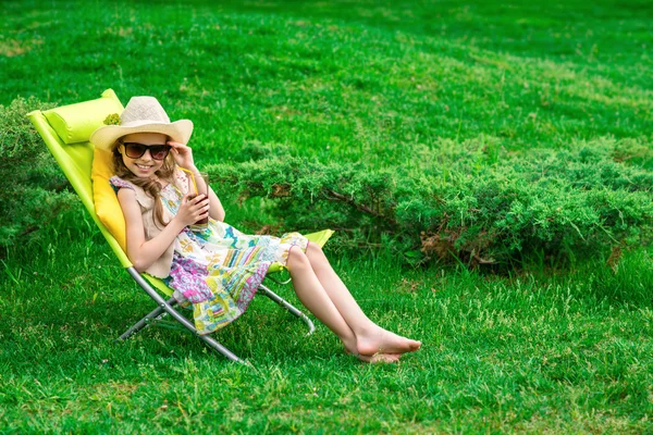 Cute girl relaxes with juice  at chair on grass. — Stock Photo, Image