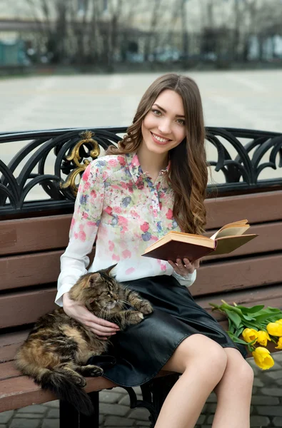 Girl reading a book with a cat on a bench in the city — Stock Photo, Image