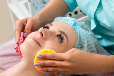 Güzel genç bir kadın yüz temizleme tedavisi görüyor. Model kozmetik cilt bakımı yaptırıyor. Kozmetik yüz masajı. Güzellik, kaplıca, kozmetoloji ve rahatlama konsepti.