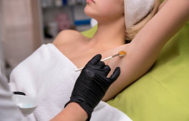 Kozmetik doktoru hastanın vücuduna saç jölesi sürüyor. Kozmetik güzellik merkezindeki bir terapistten saç çıkarma kozmetik prosedürü. Lazer epilasyon ve kozmetoloji. Şeker ve balmumu.