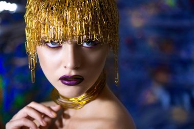 Yaratıcı makyajlı güzel bir modelin portresi ve ataçlardan altın mücevherler. Metal yaratıcı miğfer