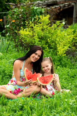 İki gülümseyen kız çiftlikte bir dilim karpuz yiyorlar. Anne ve kızı birlikte vakit geçiriyorlar. Ülke biçimi.