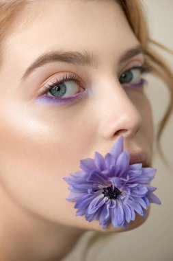 Mükemmel ciltli, renkli makyajlı ve ağzında çiçek olan güzel bir genç kadın. Yaratıcı profesyonel makyajlı bir manken. SPA, sağlık, vücut bakımı ve cilt bakımı konsepti.