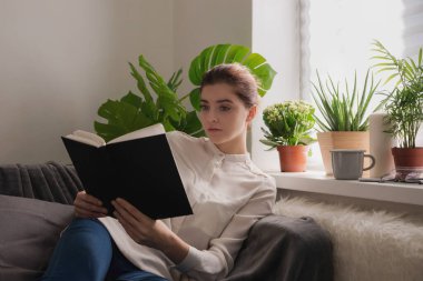 Genç kadın evde kitap okuyor. Rahatlama ve eğitim kavramı.