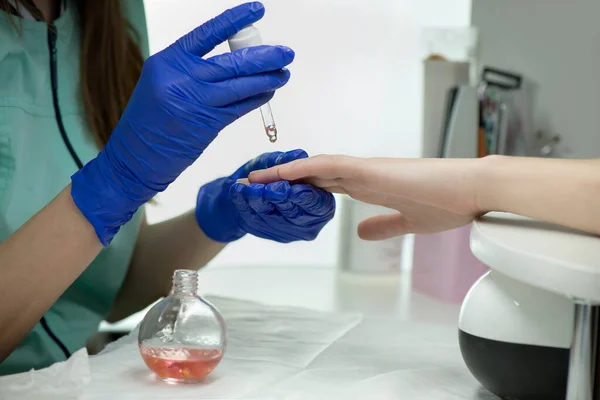 Woman hands in a nail salon receiving a classical manicure - cuticle oil procedure. Hand and nail skin care. Manicure and pedicure procedures and SPA. Close up, selective focus.