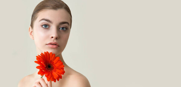 Beautiful young woman with perfect skin and flower. Fashion model face with natural make-up and red  gerbera flower in hand.  SPA, wellness, bodycare and skincare concept.