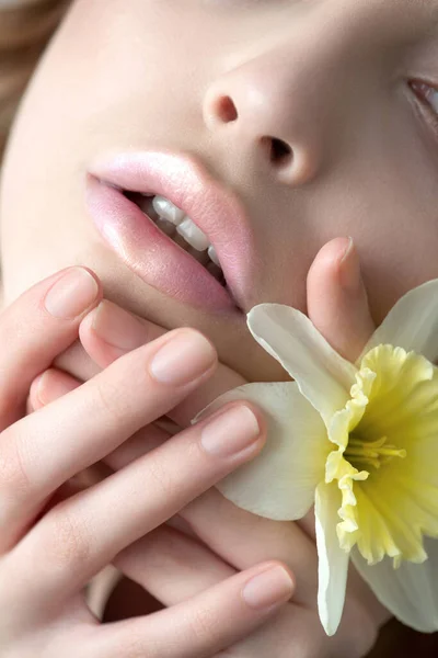 Close up of fashion model lips  with  professional holographic, radiant lip make-up.  Beautiful young woman with perfect skin, natural make up and narcissus flower. SPA, wellness  concept. Close-up, selective focus