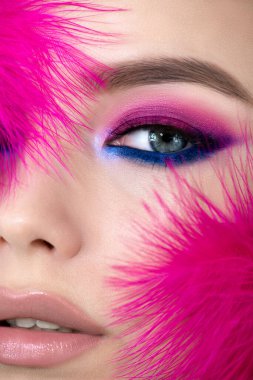 Parlak renk makyajlı güzellik modeli portresi. Profesyonel makyajı ve canlı pembe tüyleri olan güzel genç bir kadının göz kapağı. Yaklaş, seçici odaklanma.