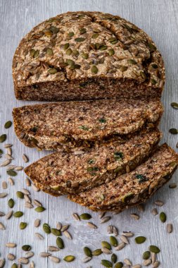 Bir somun kepekli yeşil karabuğday ekmeği dilimlenmiş balkabağı ve ahşap zemin üzerinde ayçekirdeği. Glütensiz, düşük karbonhidratlı ev yapımı ekmek. Yaklaş, seçici odaklanma.