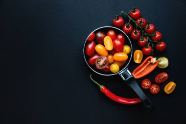 Siyah arka planda küçük tavada domates ve biber. Sağlıklı beslenme ve vejetaryen yemekleri, yemek pişirme konsepti. Dikkat çekmeyen, seçici odaklanma. Üst görünüm, düz görünüm, kopyalama alanı.