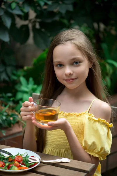 Cute little girl is drinking tea on breakfast.  Kid holds hot beverage.