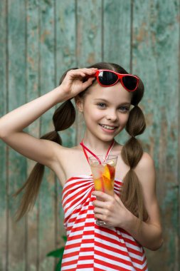 Şirin küçük kız eski kırsal ahşap arka planda limonata içiyor. Çocuk elinde bardak ve soğuk çay tutuyor. Uzayı kopyala Yaz ve tatil konsepti.