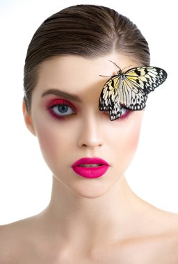 Mükemmel ciltli, uzun kirpikleri olan ve yüzünde kelebekle poz veren güzel bir genç kadın. Renkli profesyonel makyajlı moda güzellik modeli portresi. SPA ve sağlık, makyaj ve cilt bakımı konsepti.