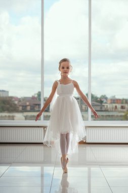 Beyaz bale kostümü ve sivri ayakkabılı şirin küçük balerin odada dans ediyor. Kid ve Bale dansı. Çocuk kız bale okuyor. Kopyalama alanı.